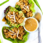 Vegan cashew tofu lettuce wraps on a white plate topped with peanut sauce