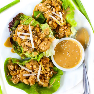 Vegan cashew tofu lettuce wraps on a white plate topped with peanut sauce