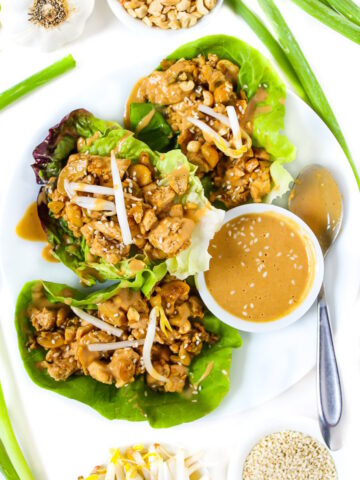 Vegan cashew tofu lettuce wraps on a white plate topped with peanut sauce