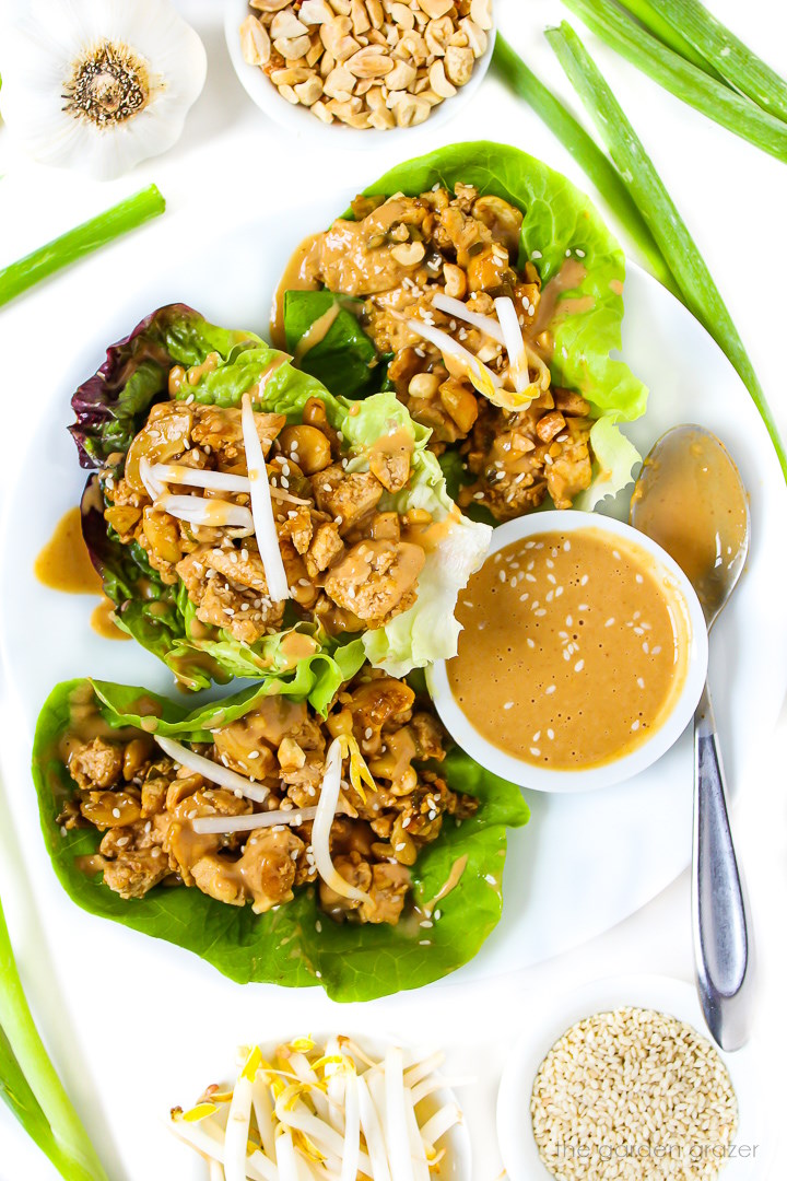 Vegan cashew tofu lettuce wraps on a white plate topped with peanut sauce