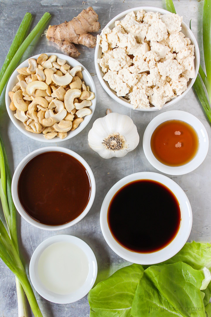Tofu, cashews, ginger, garlic, tamari, hoisin sauce, and vinegar ingredients laid out on a metal tray