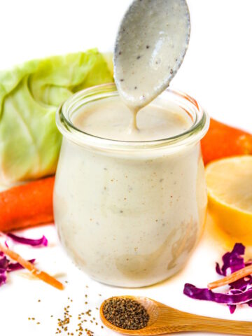 Spoon lifting out vegan coleslaw dressing from a small glass jar
