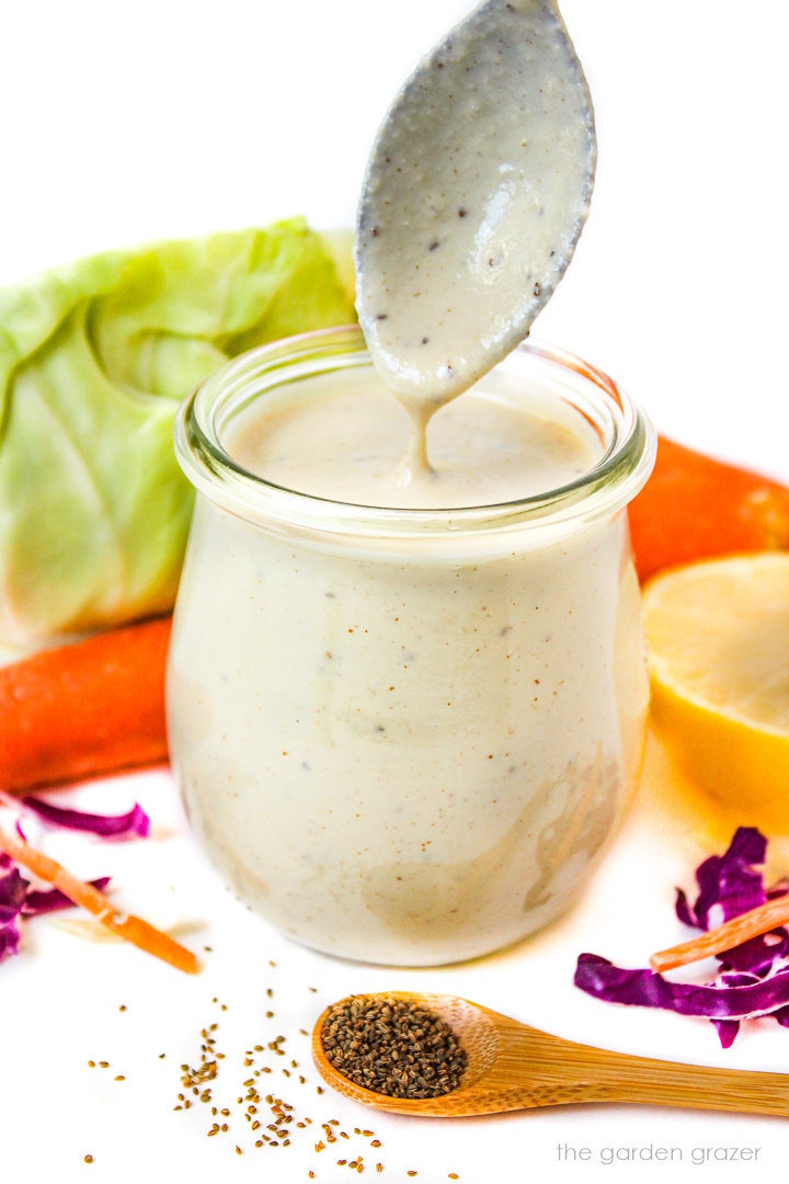 Spoon lifting out vegan coleslaw dressing from a small glass jar