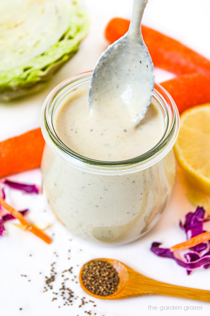 Metal spoon lifting up coleslaw dressing from a glass jar