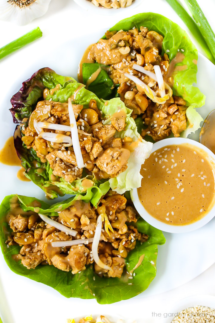 Vegan cashew tofu lettuce wraps topped with peanut sauce on a white plate