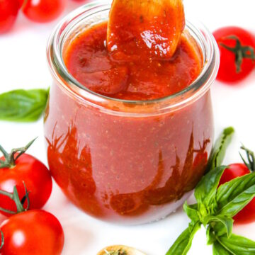 Vegan pizza sauce in a small glass jar with wooden serving spoon