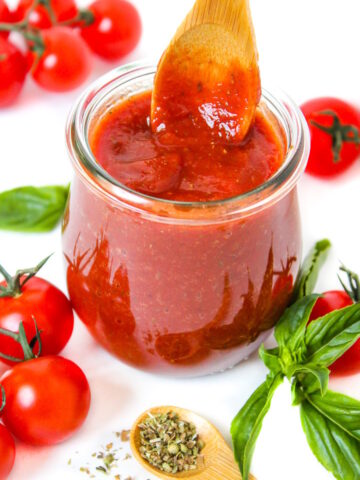 Vegan pizza sauce in a small glass jar with wooden serving spoon