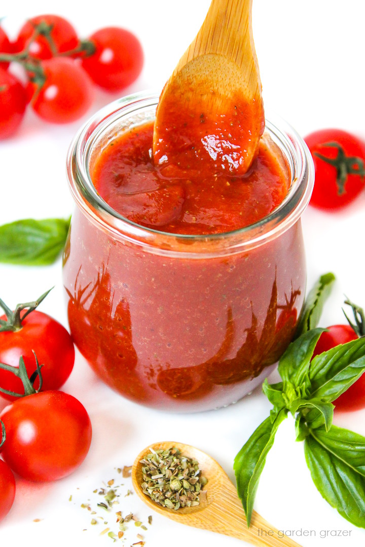 Vegan pizza sauce in a small glass jar with wooden serving spoon