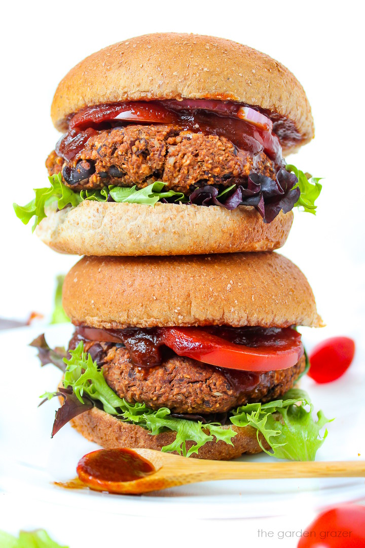 Two stacked vegan walnut burgers with toppings on a white plate