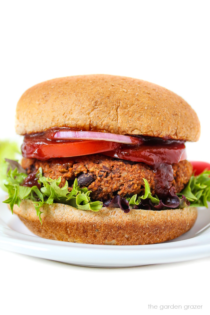Vegan black bean walnut burger on a bun with lettuce, tomato, onion, and BBQ sauce