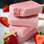 Frozen strawberry cream popsicles stacked together on a white plate with fresh strawberries