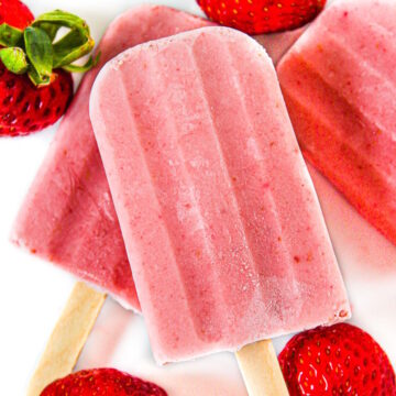 Vegan strawberry cream popsicles on a white plate with fresh strawberries