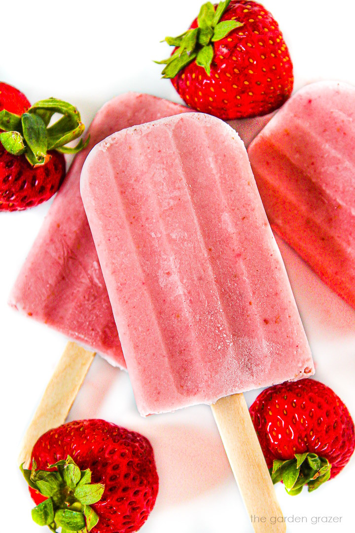 Vegan strawberry cream popsicles on a white plate with fresh strawberries