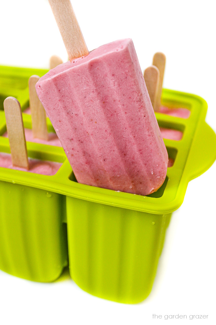 A frozen strawberry cream popsicle lifting out of a green mold