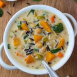 Vegan creamy butternut squash wild rice soup in a white serving bowl with spoon