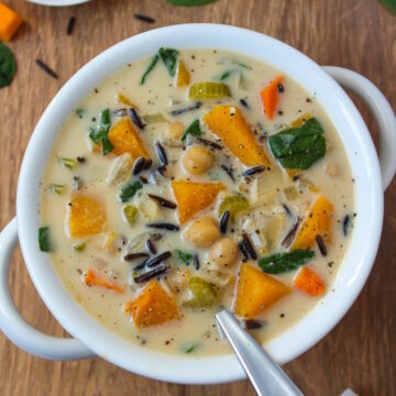 Vegan creamy butternut squash wild rice soup in a white serving bowl with spoon
