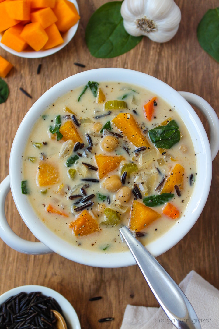 Vegan creamy butternut squash wild rice soup in a white serving bowl with spoon