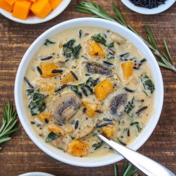 A bowl of vegan creamy butternut squash wild rice soup with kale and mushrooms on a wooden table