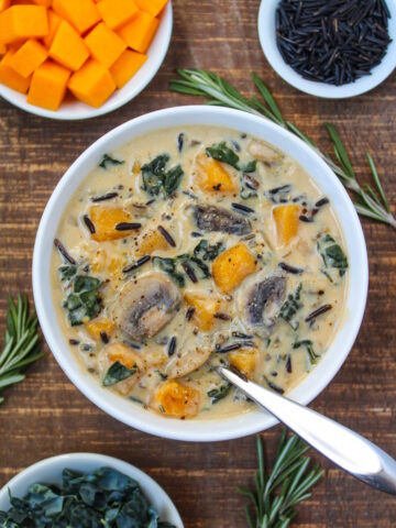 A bowl of vegan creamy butternut squash wild rice soup with kale and mushrooms on a wooden table