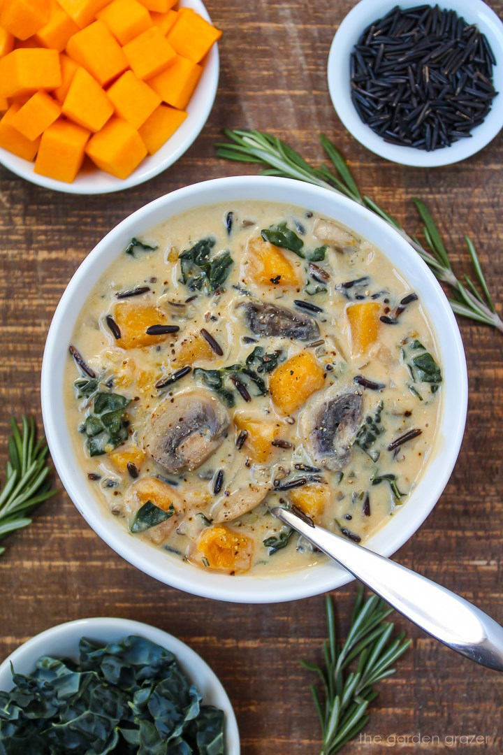 A bowl of vegan creamy butternut squash wild rice soup with kale and mushrooms on a wooden table