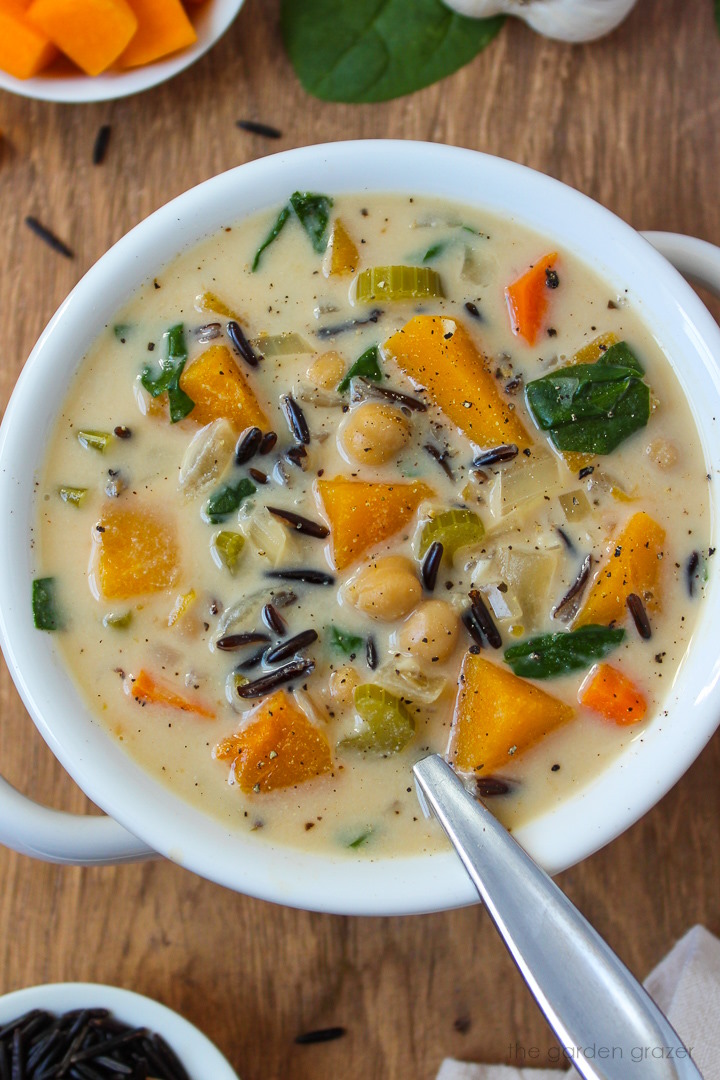 Close up view of creamy butternut squash wild rice soup in a white serving bowl with spoon