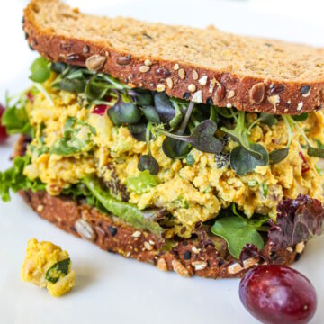 Curried chickpea salad sandwich on a white plate with grapes