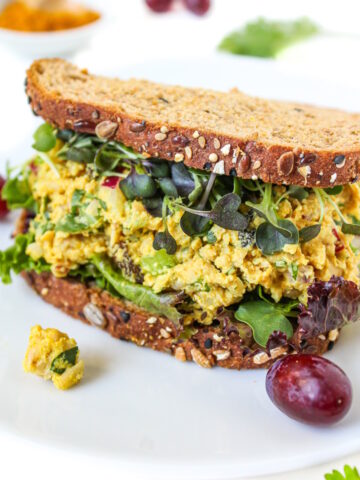 Curried chickpea salad sandwich on a white plate with grapes