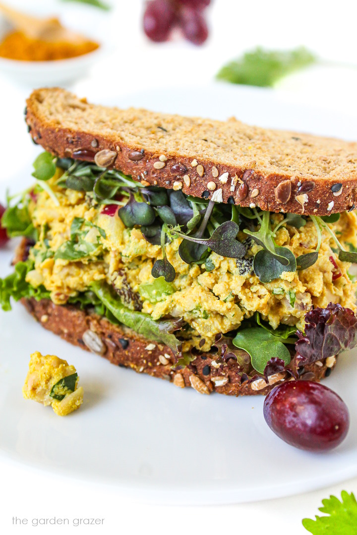 Curried chickpea salad sandwich on a white plate with grapes