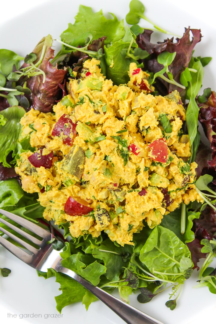 Curried chickpea salad on top of fresh baby greens on a white plate with fork
