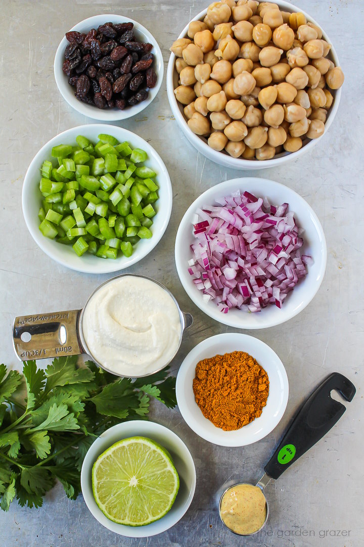 Garbanzo beans, celery, red onion, mayo, raisins, and curry spice ingredients laid out on a metal tray