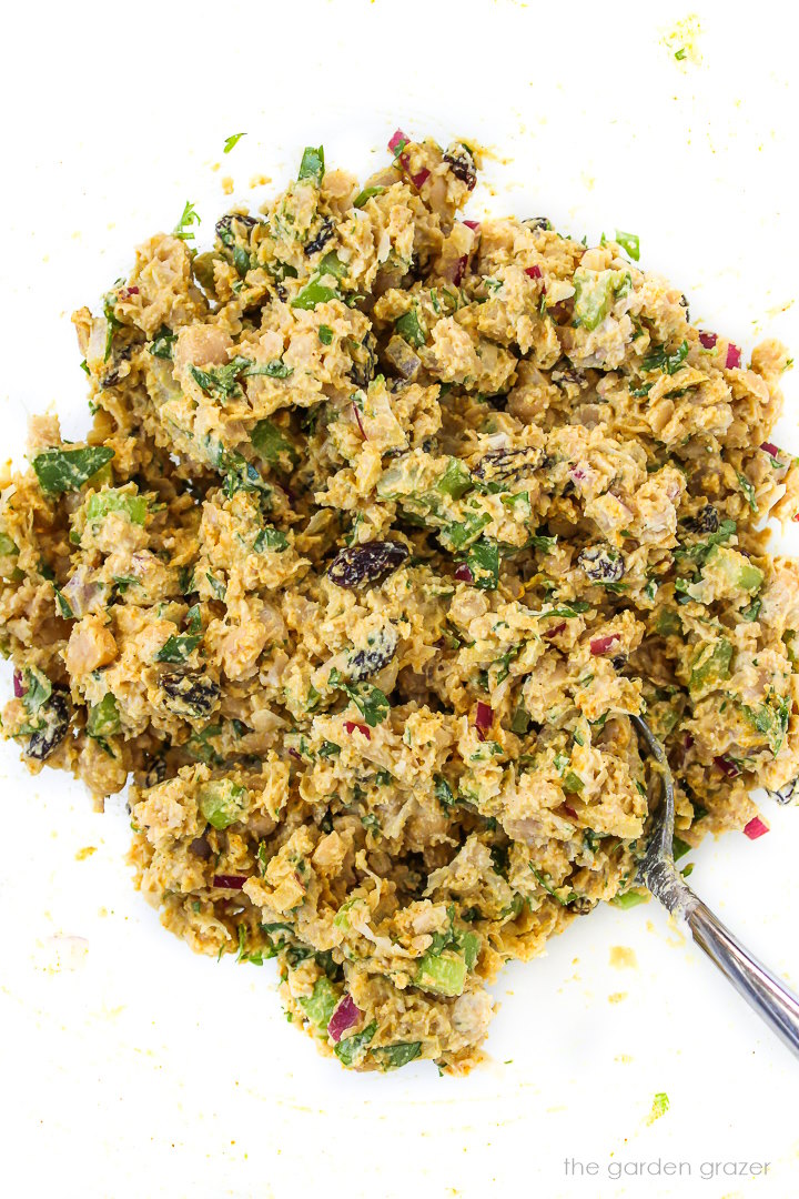 Curried chickpea salad mixed together in a glass bowl with metal spoon