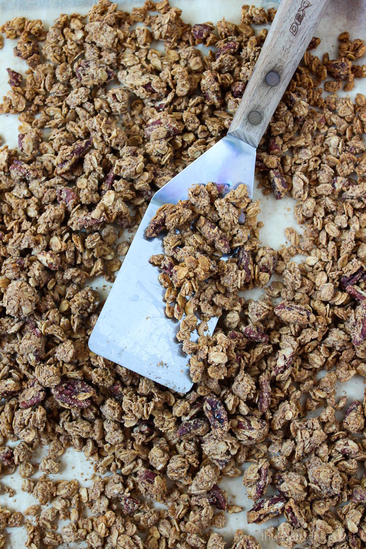 Metal spatula scooping up Pumpkin spice granola on a sheet pan after baking