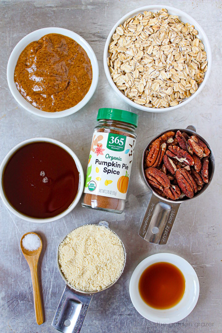 Rolled oats, almond butter, spices, pecans, syrup, and almond flour ingredients laid out on a metal tray