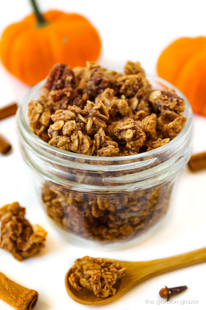 Close up view of pumpkin pie spice granola in a glass jar with little pumpkins in the background