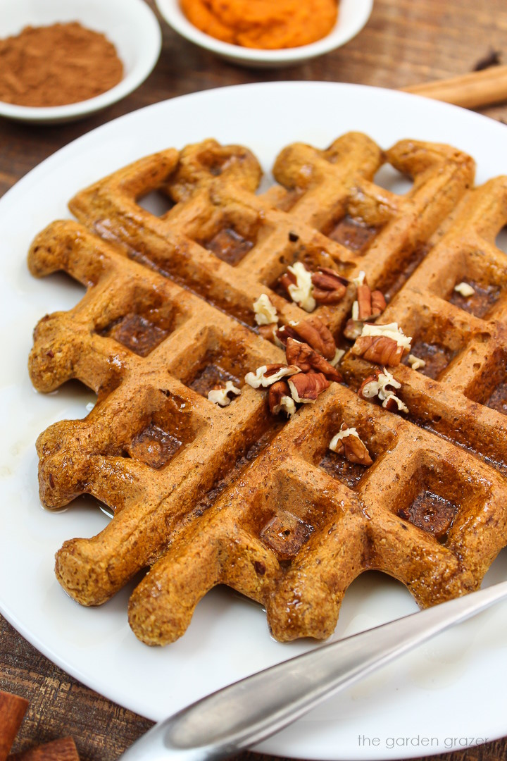 Close up view of vegan pumpkin waffle on a plate topped with pecans