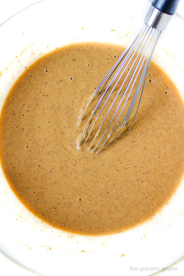 Overhead view of waffle batter mixed together in a large bowl with whisk