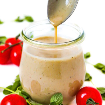 A spoon lifting out vegan Greek dressing from a small glass jar