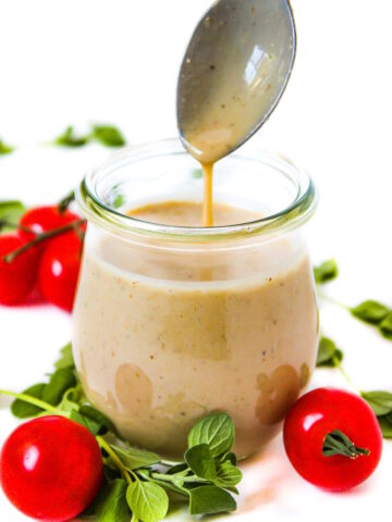 A spoon lifting out vegan Greek dressing from a small glass jar