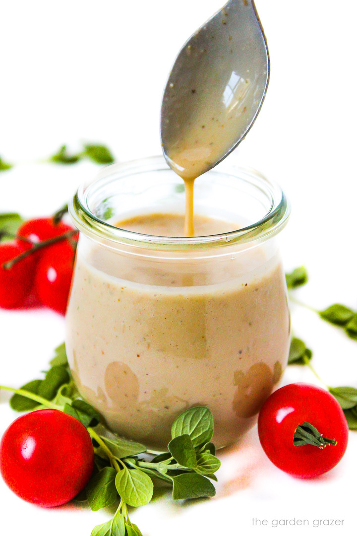 A spoon lifting out vegan Greek dressing from a small glass jar