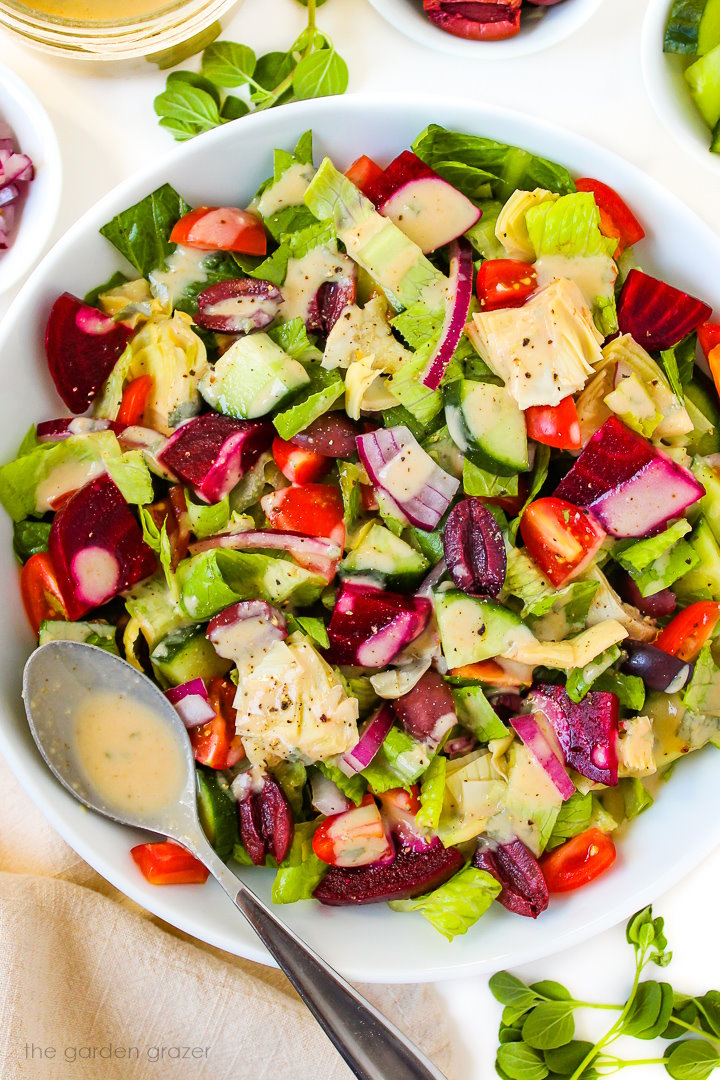 Close-up view of Vegan Greek Salad in a white bowl with spoon for dressing