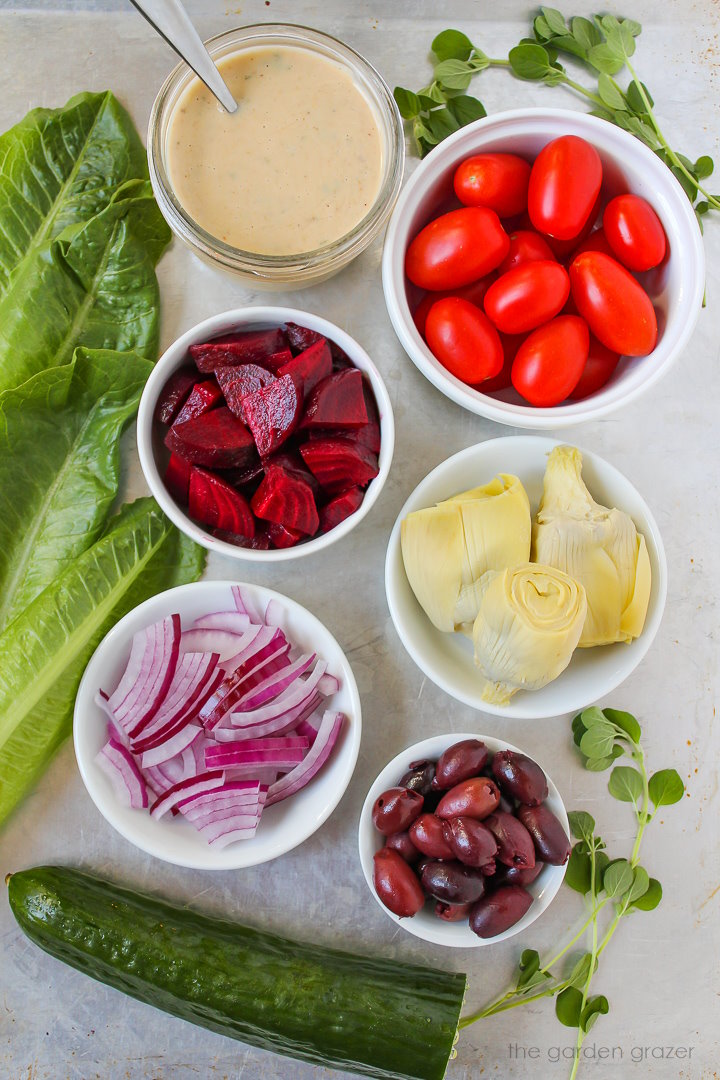 Romaine lettuce, tomatoes, beets, red onion, artichoke hearts, and cucumber ingredients laid out on a metal tray