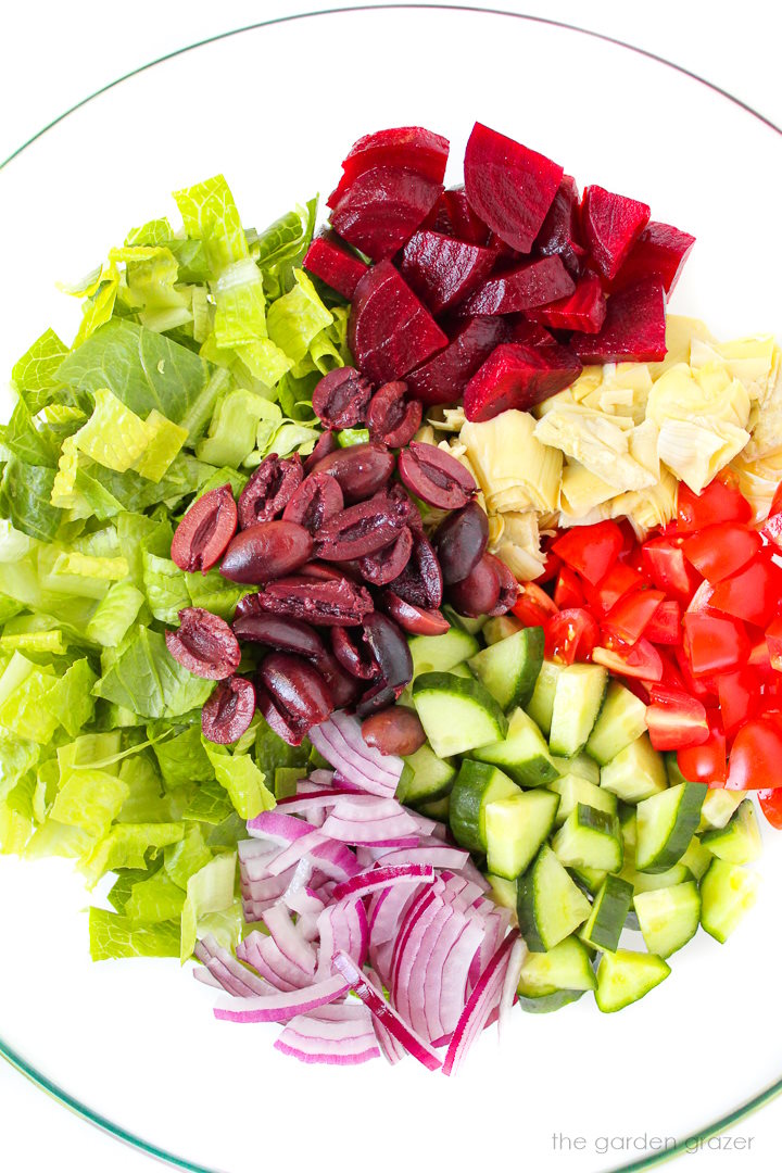 Overhead view of ingredients in a bowl for Vegan Greek Salad before tossing together