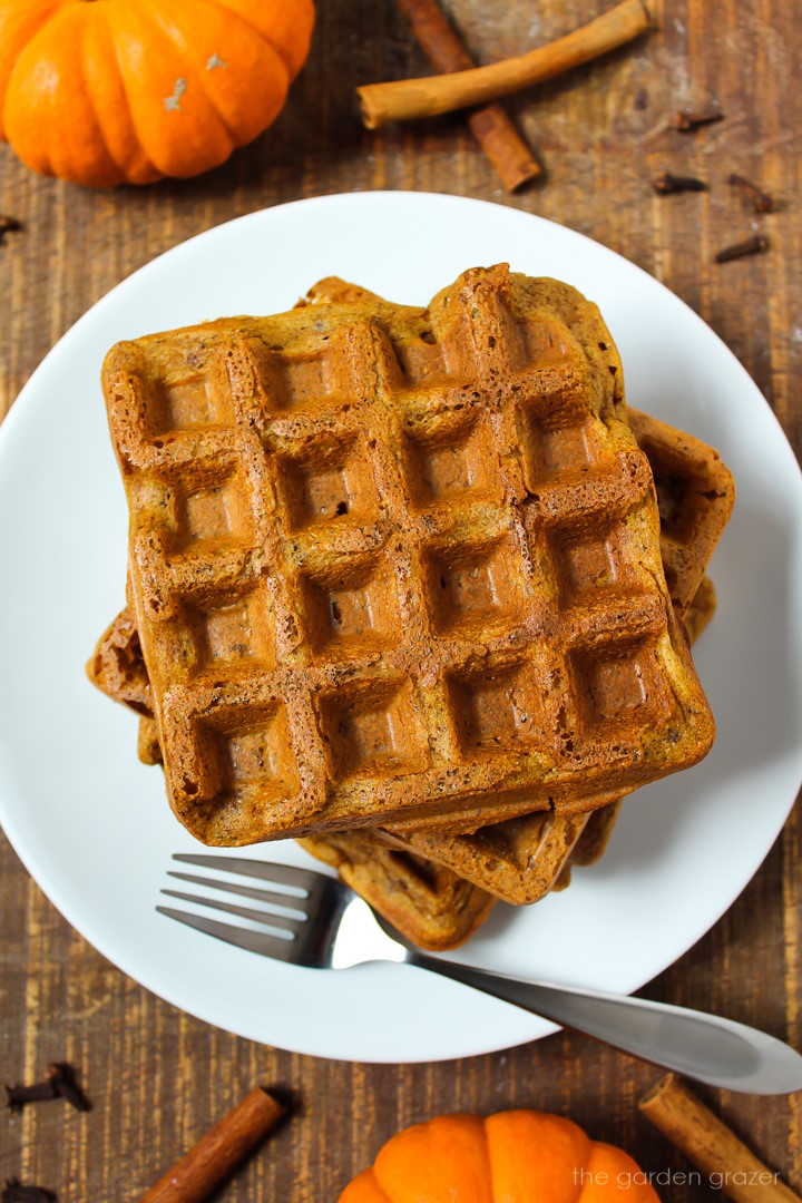Vegan pumpkin waffles stacked on a white plate with serving fork