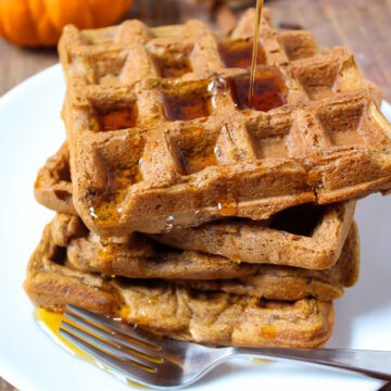 Maple syrup being drizzled over vegan pumpkin waffles on a white serving plate