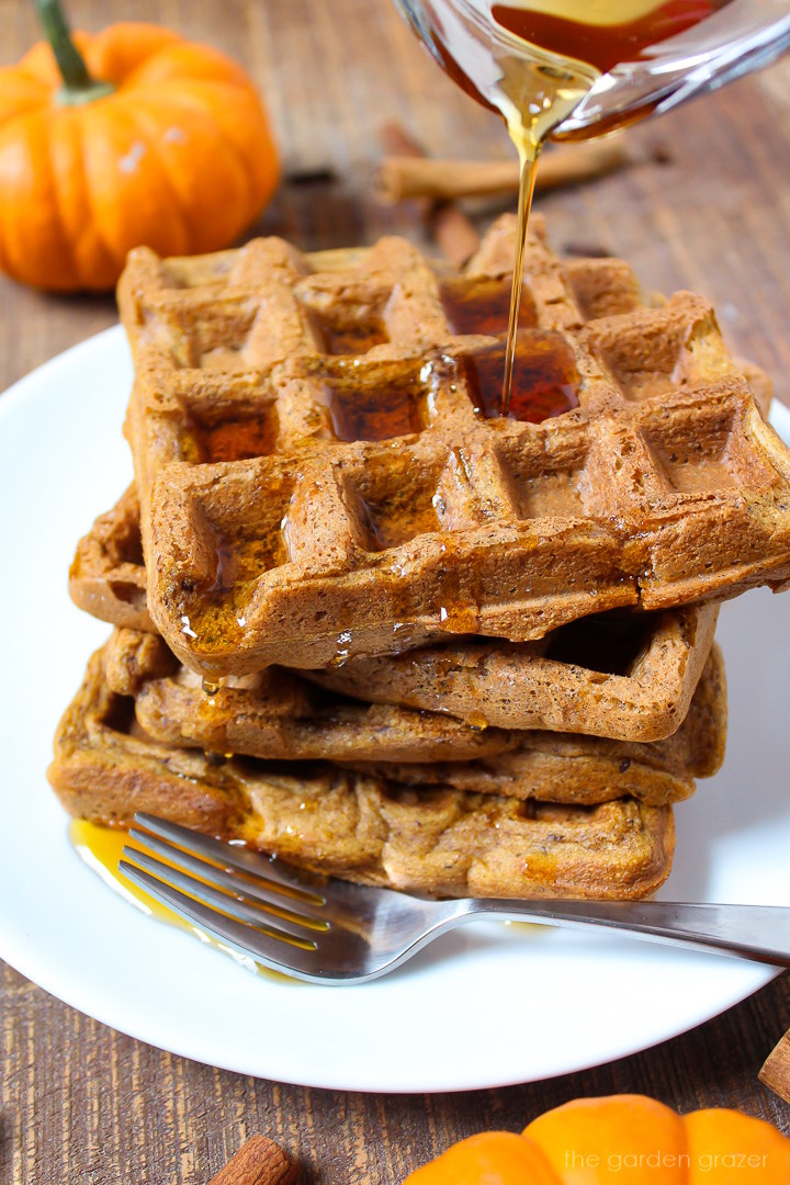 Maple syrup being drizzled over vegan pumpkin waffles on a white serving plate
