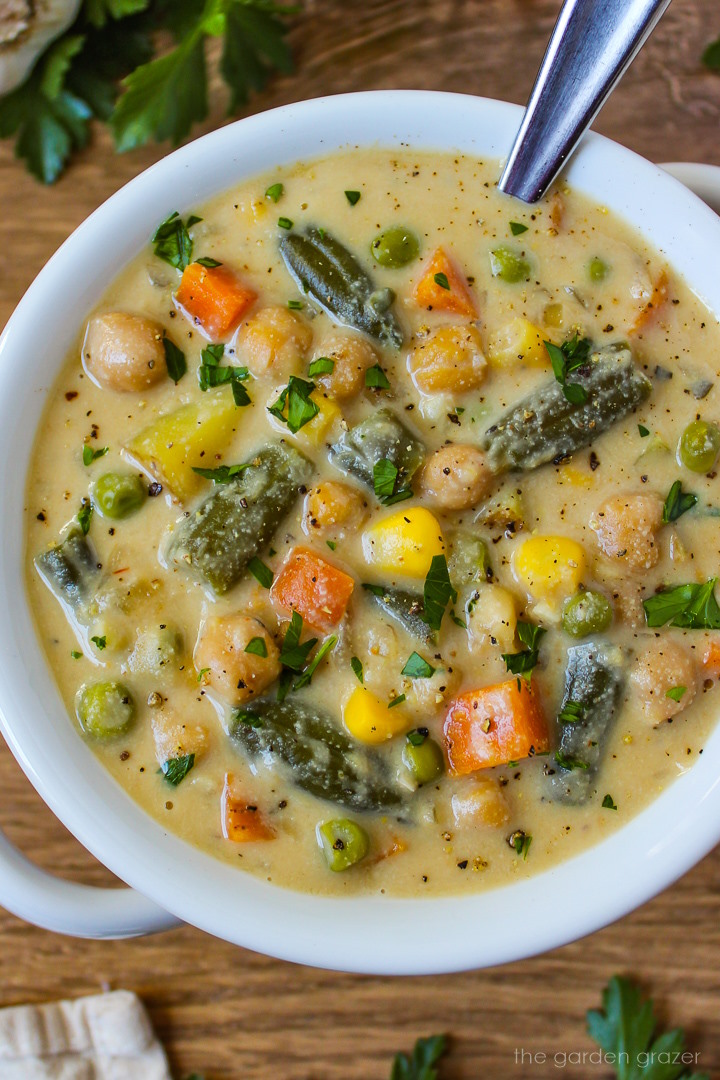 Close up view of vegan vegetable chowder in a white serving bowl with spoon