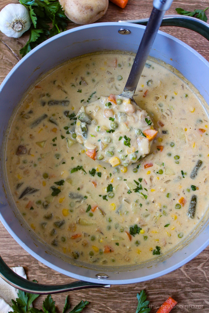 A soup ladle lifting up vegan vegetable chowder from a cooking pot