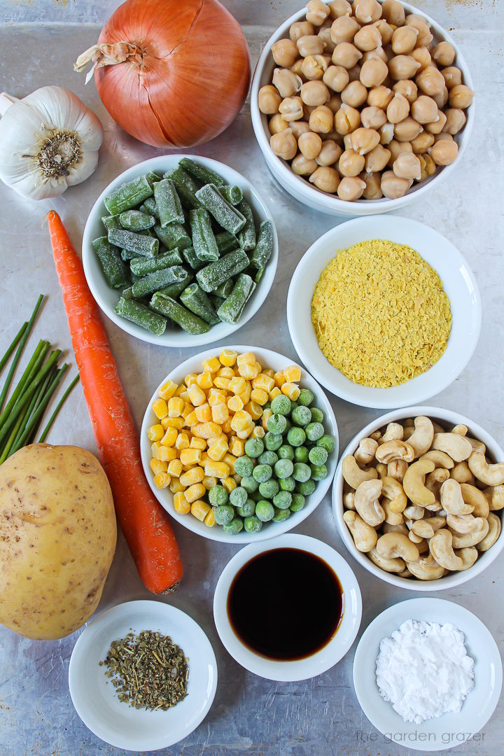 Chickpeas, onion, potato, carrot, and frozen vegetables ingredients laid out on a metal tray