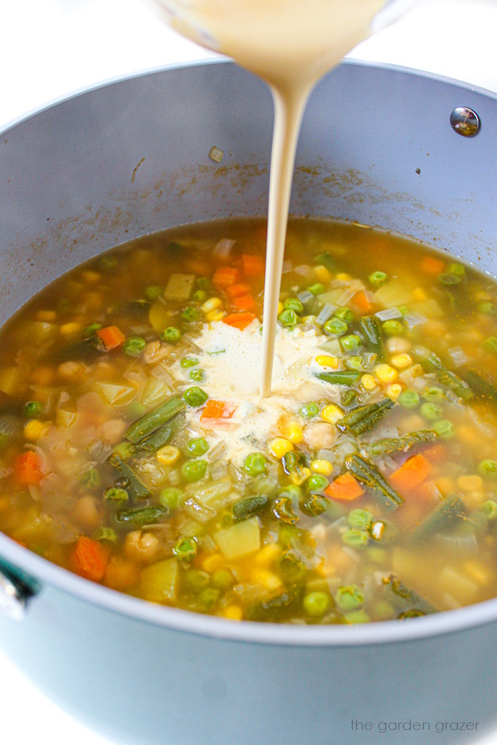 Blended cashew cream being poured into a pot of chowder