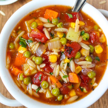 Vegan vegetable orzo soup in a small white bowl with fresh parsley